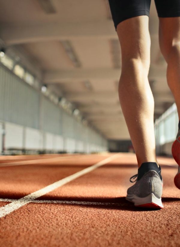 From below back view of crop strong runner walking along running track in athletics arena while doing warm up exercises during workout